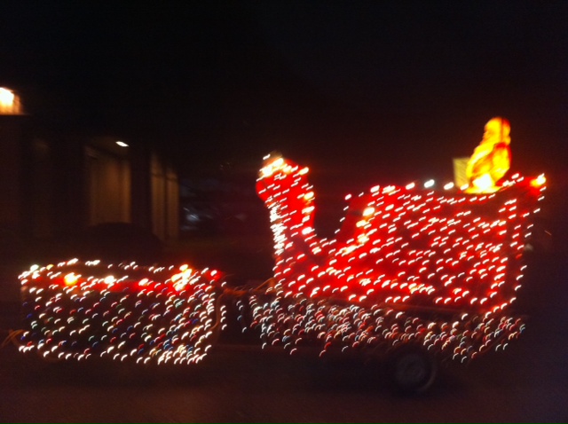 lighted tractor decorated as a red sleigh outlined in white lights with Santa riding it