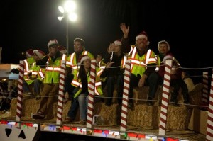 Participants in Santa hats wave from aboard a float with red-and-white candy-cane striped poles.