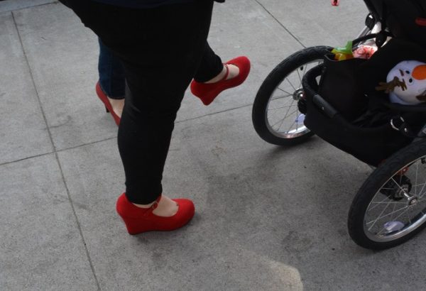 Woman's red high heels as she takes a playful step kick forward behind a baby carriage