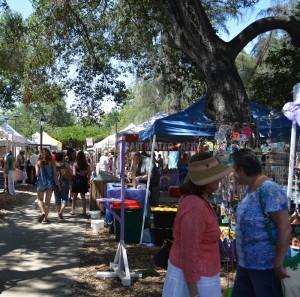 Man and woman look at a line of tented booths selling crafts in Libbey Park at Lavender Festival
