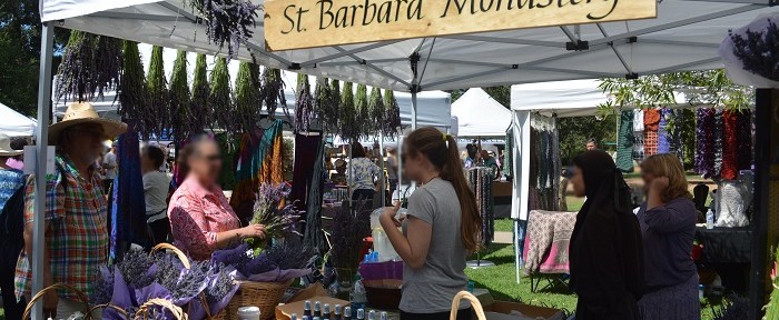 Shoppers browse bunches of lavender in a white tented exhibit with a sign that says, "St. Barbara Monastery"