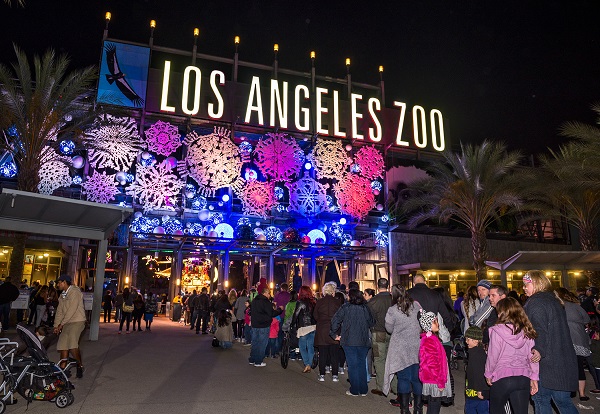 Attendees stand in line at front gate with "Los Angeles Zoo" sign lit up with red, white and blue snowflakes at night