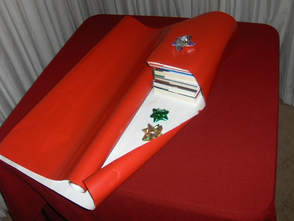 Stack of books being wrapped in red wrapping paper with green and gold bows