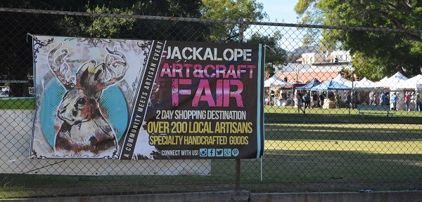 Jackalope Fair sign on chain link fence with crafters' tents beyond it.