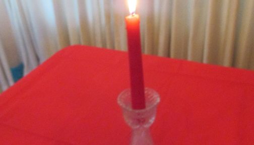 Red candle in cut-glass holder burns on as it sits on red tablecloth