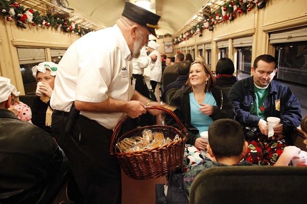 Conductor serves cookies to passengers in Christmas-decorated vintage train car