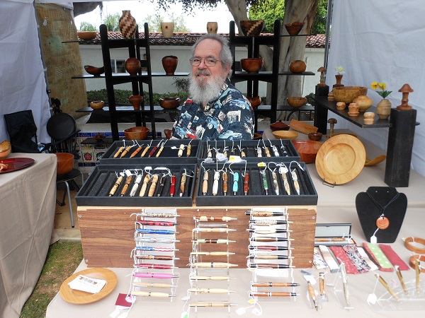 Artist J. Michael Evens in his art booth at a craft fair, surrounded by his hand-turned wooden pens, platters and bowls