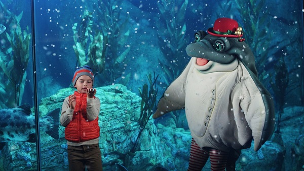 Small boy examines snowflakes next to costumed "sea skate" character in the Blue Cavern