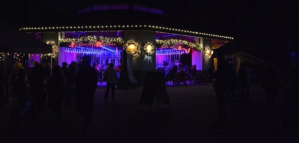 Carousel glows with Christmas lights through crowd