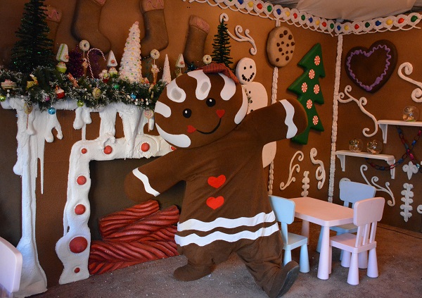 Costumed "gingerbread" character dances next to a mantel trimmed to look like gingerbread