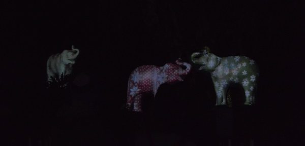 Cement elephants on which light patterns of polka dots and stripes are being projected at LA Zoo Lights
