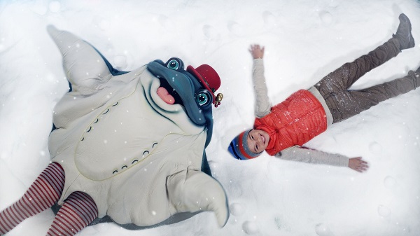Sea skate character and small boy make snow angels in the snow play area
