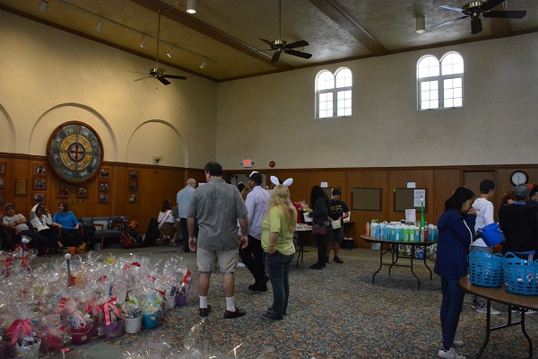 Volunteer with white bunny ears stands in the cneter of church hall with other volunteers and Easter baskets