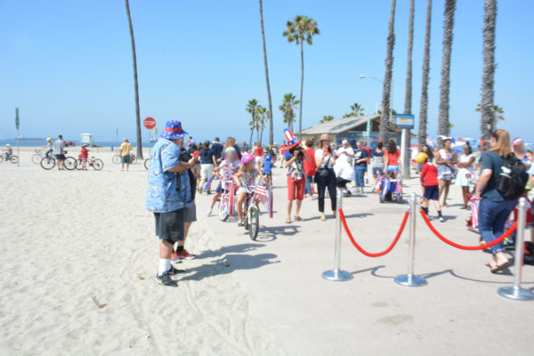 Bike riders congregate near red ropes to signal start of bike parade at the beach