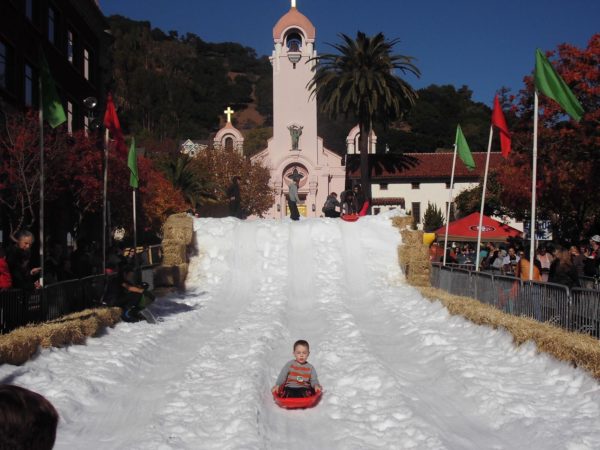 Child on a sled coming down a snow-covered surface near a mission