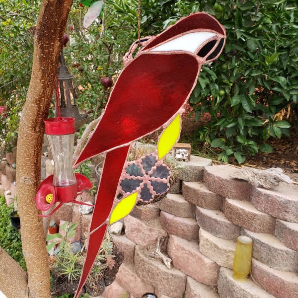 red stained-glass parrot in back yard near brick wall
