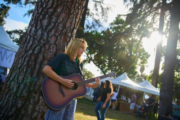 Blonde woman plays guitar under a tree with Jackalope tents in the background