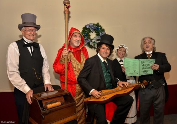 Carolers in Dickensian clothing sing Christmas carols around an 1895 organ