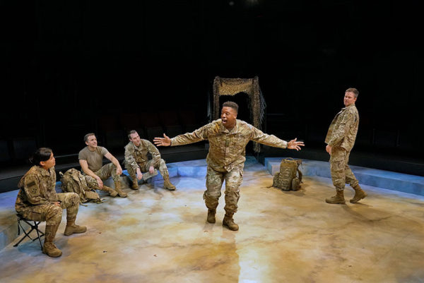 Douglas Miller (DeLeon Dallas), in combat uniform, spreads his arms and sings center stage as three other uniformed soldiers sit around him in a half-circle and Aaron C. Finley, as Staff Sergeant Mike Randolf, stands looking on from stage left 