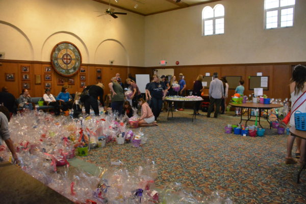 Long shot of fellowship hall with completed Easter baskets on floor and volunteers at tables to create more