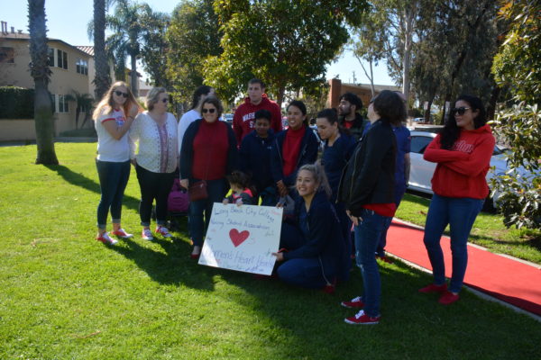 Group of Long Beach City College nursing students poses on red carpet with sign with a red heart in the center
