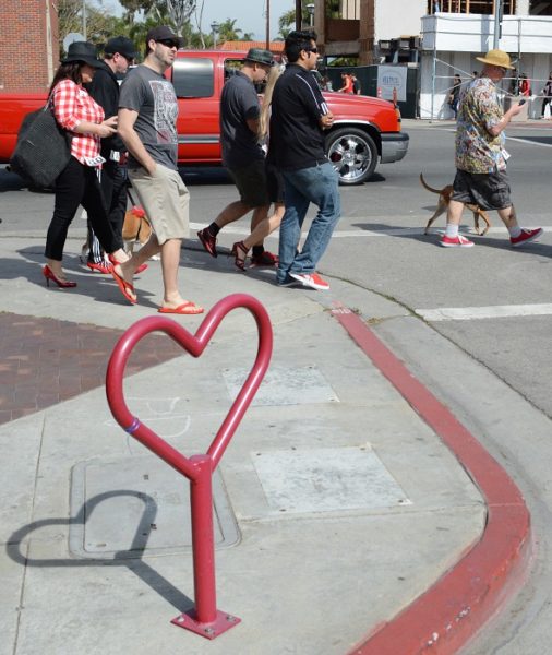 Walkers in red shoes on Long bBeach street, passing a red iron heart sculpture 