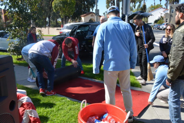 Two volunteers roll out a red carpet on the sidewalk near Livingston Park