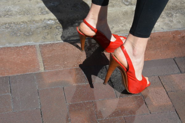 Closeup of woman's feet as she wears red high heels and jeans and poses on tile