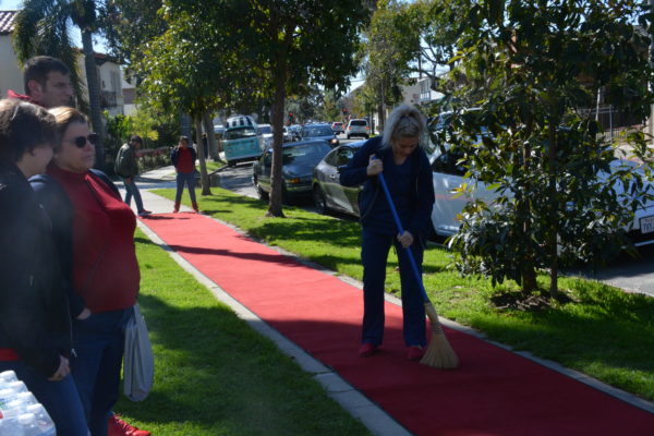 Woman sweeps the "red carpet" runner laid on a sidewalk