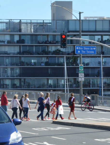 Group of walkers in red shoes, led by beauty queen in sash and tiara, crosses street