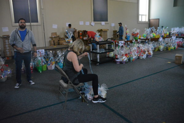 Woman cuts ribbon in center of room to wrap baskets as completed baskets sit on table at "Operation Easter Basket"