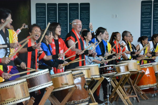Group of about 15 people in red vests play Japanese drums inside the Aquarium of the Pacific