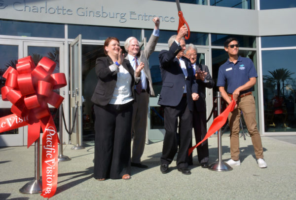 Dr. Schubel holds red-handled giant scissors aloft as Councilmember Pearce cclaps, Doug Otto pumps a fist in the air and Steve Morikawa smiles after ribbon is cut