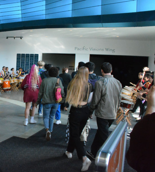 Students file towards a room labeled "Pacific Visions Wing" as taiko drummers play