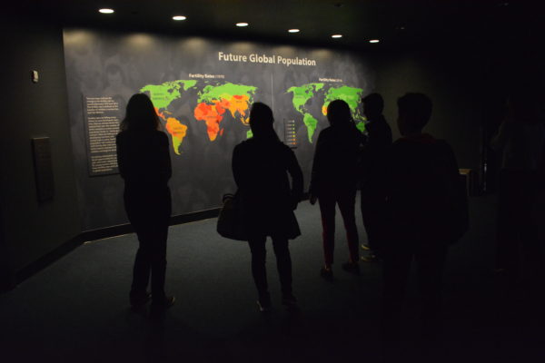 Students silhouetted against screen with world map showing population growth