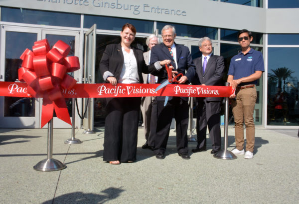 Dr. Jerry Schubel, Aquarium of the Pacific President, wields a large pair of scissors over a red ribbon with white letters spelling out "Pacific Visions" stretched before the Aquarium entrance. He's flanked by Aquarium Board Vice Chair Doug Otto, American Honda Vice President of Corporate Relations and Social Responsibility and Aquarium Board Director Steve Morikawa, and Long Beach Councilmember Jeannine Pearce