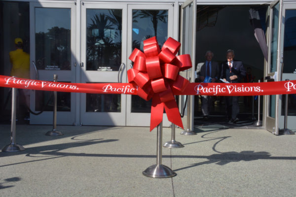 Dr. Jerry Schubel and Doug Otto framed in the door of the Aquarium on the Pacific, on their way out as a giant red ribbon with "Pacific Visions" on it in white, and a red bow on a stanchion, stands before the door