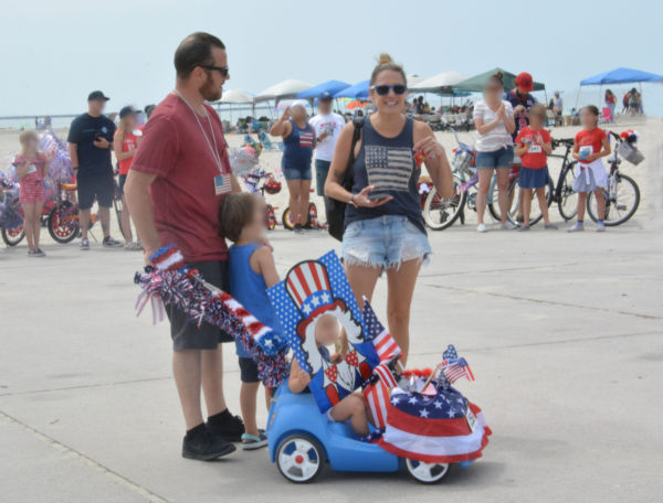 Couple with a baby in a stroller decorated with an "Uncle Sam" banner with a hole for the baby's face smile for the camera