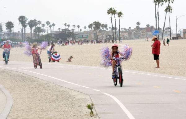 Young girl on a bike with red-white-and-blue tinsel "wings" on either side of it