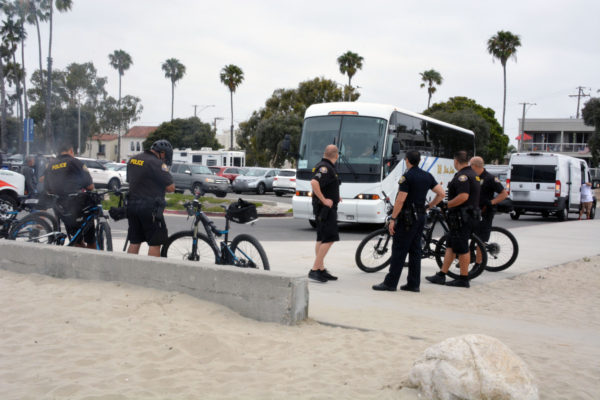 Six police officers staand near the parking lot with their bicycles as a tour bus pulls in