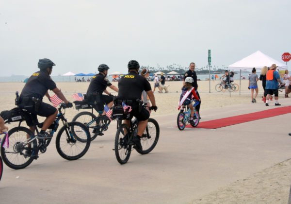 Three police officers ride their bikes towards a "red carpet" on the sand just adjacent to the bike path