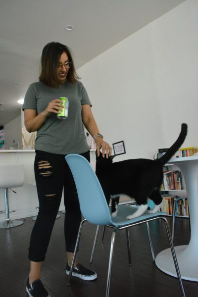 Tushita pets a black and white "tuxedo" cat as he stands on a chair
