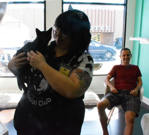Volunteer with cat ears smiles as she holds a black cat in her arms