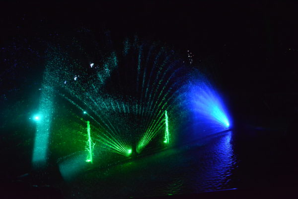 Plumes of water fan out in various directions, with green and blue lights behind them