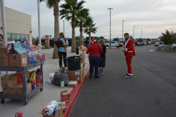 Justin Rudd, in red Santa suit, stands near OC Animal Care staffers near a pile of donations