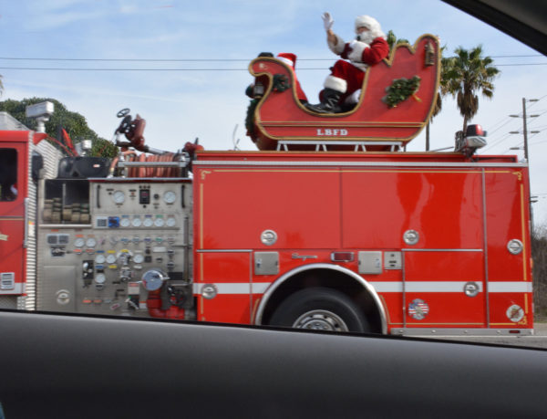 Santa waves from a red sleigh with "LBFD" on it, on the back of a fire engine