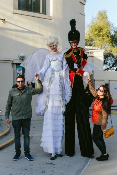 Father and daughter pose with a princess in a white dress, on stilts, and a costumed "toy soldier", also on stilts