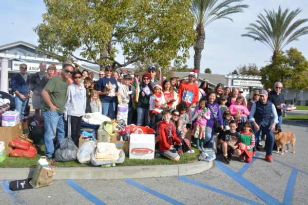 Group for Operation Santa Paws smiles outside Long Beach ACS shelter next to pile of pet food and toys