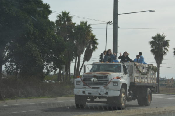 Staffers wave from the flatbed of a white truck decorated with Christmas greens