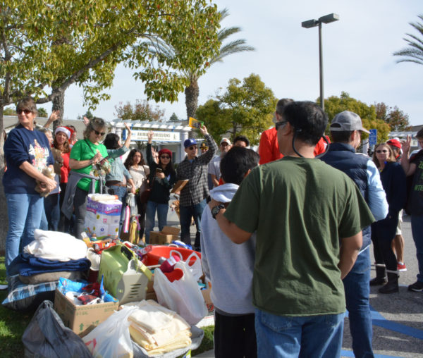 Volunteers take selfies and stand near a pile of pet food, treats, leashes, dishes and supplies outside Long Beach ACS